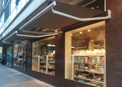 Toldo de brazos articulados instalado en fachada de local comercial, aportando sombra y protección solar al escaparate